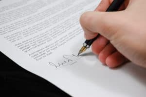 יד מחזיקה עט ומנחת על חוזה על מנת לחתום עליו